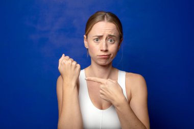 Sarışın kadın sabırsız ve kızgın görünüyor, saati gösteriyor, dakiklik istiyor, zamanında gelmek istiyor.