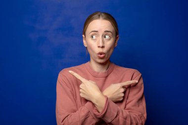 Sarışın kadın şaşkın ve şaşkın görünüyor, güvensiz ve şüpheyle zıt yönleri işaret ediyor.