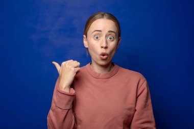 Sarışın kadın inançsızlıktan şaşkın şaşkın bakıyor, yan taraftaki objeyi işaret ediyor ve diyor ki: