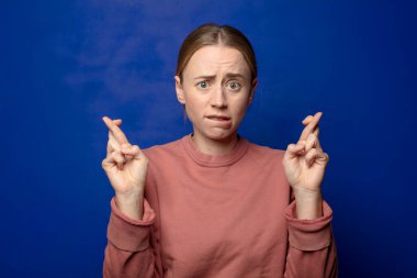 Sarışın kadın endişeyle dua ediyor ve endişeli bir bakışla iyi şanslar diliyor.