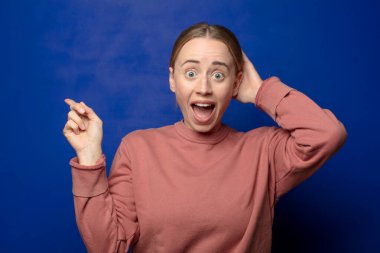 Sarışın kadın gülüyor, mutlu, pozitif ve şaşırmış görünüyor. Yan fotokopi alanını işaret eden harika bir fikrin farkına varıyor.