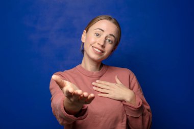 Sarışın bir kadın mutlu ve aşık, bir eli kalbinin yanında gülümsüyor ve diğer eli önde uzanıyor.