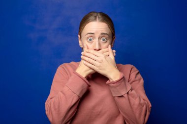 Sarışın kadın elleri ile ağzını kapatıyor, şok olmuş, şaşırmış bir ifadeyle, sır saklıyor ya da 