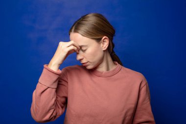 Sarışın kadın stresli, mutsuz ve hayal kırıklığına uğramış, alnına dokunuyor ve şiddetli baş ağrısı çekiyor.