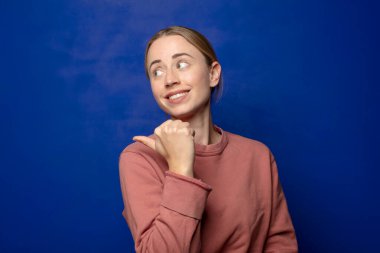 Sarışın kadın neşeyle gülümsüyor ve yan taraftaki fotokopi alanını gösteriyor, mutlu ve tatmin olmuş hissediyor.