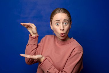 Sarışın kadın mutlu ve şaşırmış hissediyor, şok olmuş bir ifadeyle gülümsüyor ve elinde bir şey tutuyor.