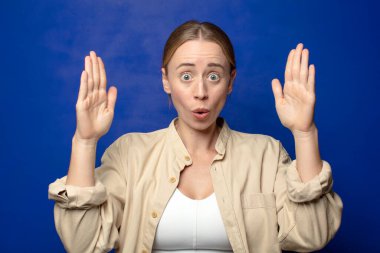 Sarışın kadın iki eliyle bir nesne tutuyor, bir nesneyi gösteriyor, sunuyor ya da reklamını yapıyor.