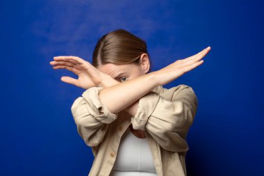 Sarışın kadın yüzünü eliyle kapatıyor ve kamerayı durdurmak için diğer elini öne koyuyor, fotoğraf ya da resimleri reddediyor.