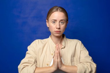 Sarışın bir kadın endişeli, umutlu ve dindar, sadık bir şekilde avuç içiyle dua ediyor, af diliyor.