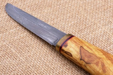 Soyut dalga paterni Şam çelik ve ahşap el yapımı Fin bıçakla geleneksel eski bir çuval arka plan üzerinde işlemek. 