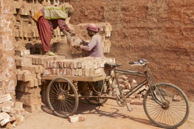 Two workers load bicycle with bricks in Dhaka, Bangladesh. clipart