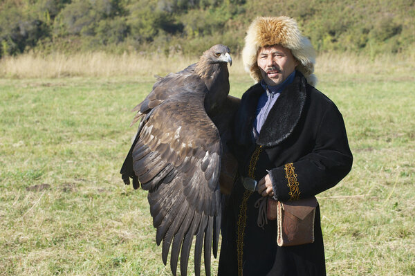 Mongolian hunter in a traditional dress holds golden eagle circa Almaty, Kazakhstan.
