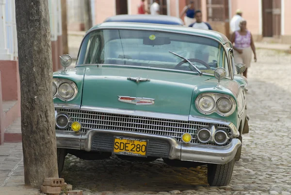La gente pasa por autos americanos antiguos estacionados en la calle en Trinidad, Cuba . —  Fotos de Stock