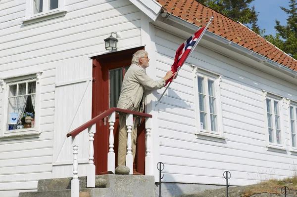 男は Skudeneshavn、ノルウェーの彼の家で国旗を修正します。. — ストック写真