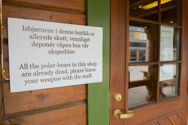 Informacje znak przy wejściu do sklepu z pamiątkami w norweskim i angielski pouczając nie wejść z broni w Longyearbyen, Norwegia. — Zdjęcie stockowe
