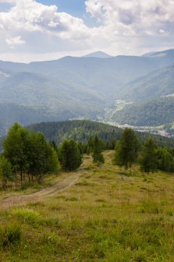 Dağlar yeşil ağaçlar ve mavi gökyüzü bulutlu