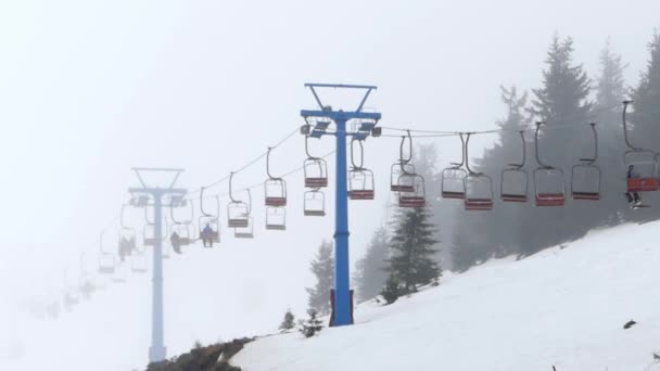 Silla elevadora en la niebla transportando a la gente a la cima de la montaña . — Vídeos de Stock