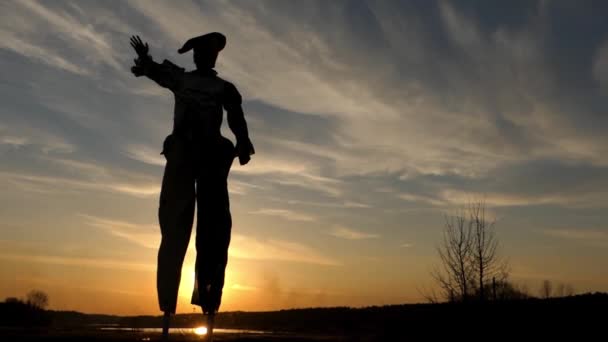 Stilt Walker no pôr-do-sol acenando com a mão no sol . — Vídeo de Stock