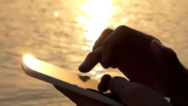 Uso de la mano Teléfono táctil al atardecer cerca del agua . — Vídeos de Stock