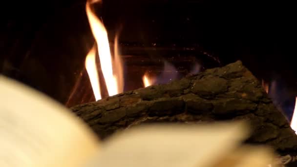 Leer un libro delante de una chimenea Primer plano . — Vídeo de stock