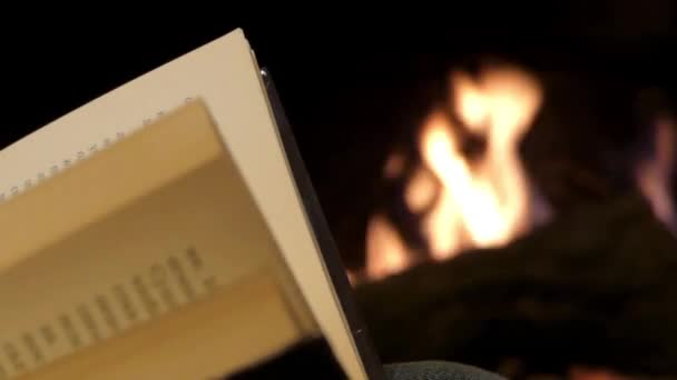 Leyendo un libro cerca de una chimenea. Páginas de giro a mano . — Vídeo de stock