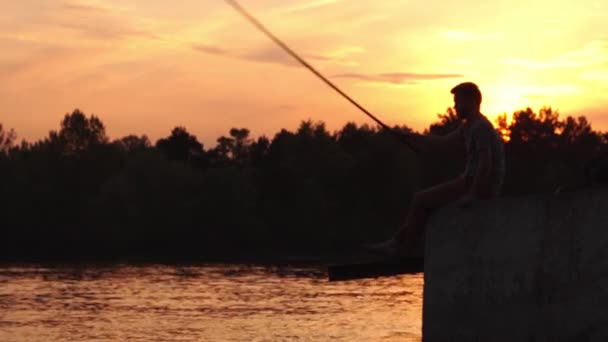 El Pescador se sienta en el muelle y la pesca. Puesta de sol . — Vídeos de Stock