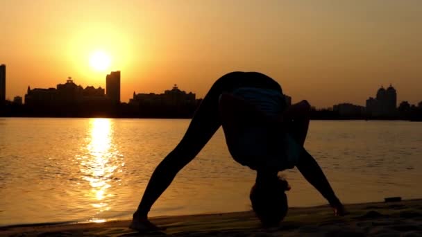 Dziewczyna praktyki jogi szeroko nogami zginania do przodu. Akcja o zachodzie słońca na plaży. — Wideo stockowe