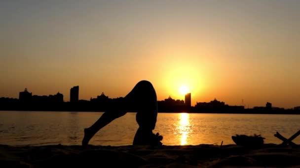 Menina faz um headstand no pôr do sol perto do rio . — Vídeo de Stock