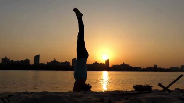 Menina faz um headstand no pôr do sol perto do rio . — Vídeo de Stock