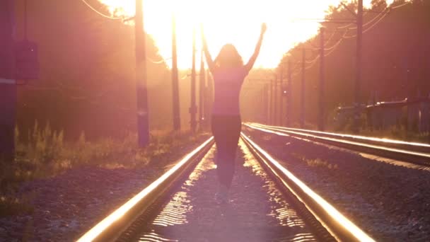 Slender Girl camina en un ferrocarril y levanta sus manos. Puesta de sol . — Vídeos de Stock
