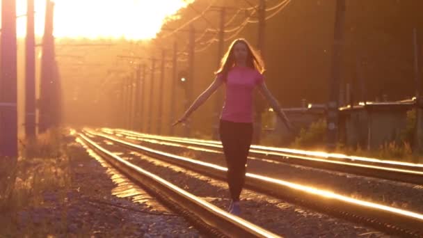 Slender Girl camina en un ferrocarril y levanta sus manos. Puesta de sol . — Vídeos de Stock