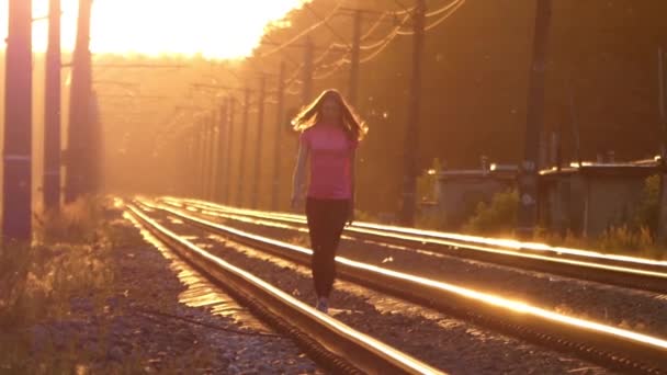 Fille mince marche sur un chemin de fer et lève les mains. Coucher de soleil . — Video