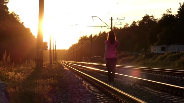 Slanke meisje loopt op een spoorlijn bij zonsondergang. — Stockvideo
