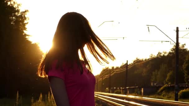 Молодая девушка в медленном движении пригибает голову и играет с волосами. действие происходит на закате — стоковое видео