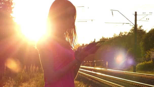 Красива дівчина довговолосий використовує телефон на заході сонця. — стокове відео