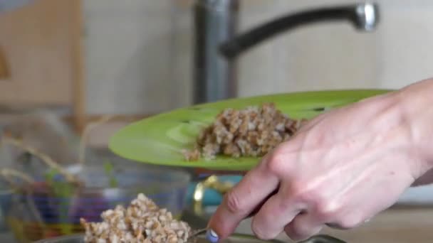 Рука наливает гречневую кашу из горшка в зеленую тарелку . — стоковое видео