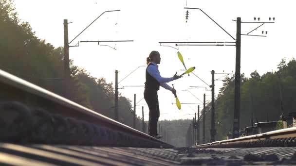 Un tipo haciendo malabares en las vías del tren. A cámara lenta. Puesta de sol. Equilibrio del ferrocarril . — Vídeos de Stock