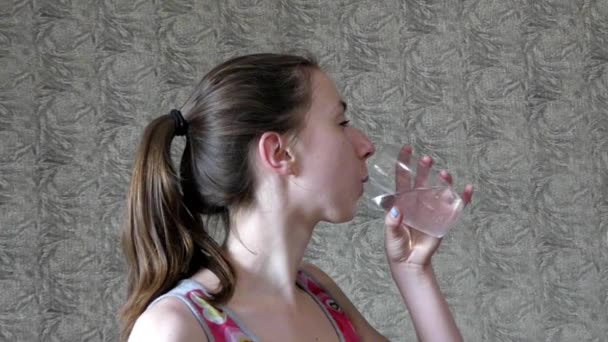 Menina jovem e bonita bebe água de um copo em câmera lenta. Fechar . — Vídeo de Stock