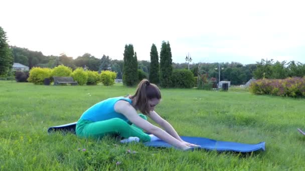 Спортивная девушка делает упражнения в парке. Сидящая позиция . — стоковое видео