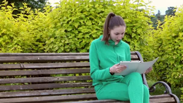 Flickan satt på en bänk som njuter av nyheten att hon såg i Tablet. — Stockvideo