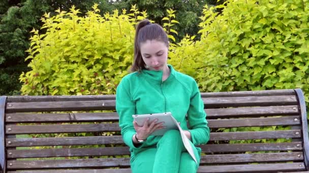 Chica sentada en un banco disfrutando de las noticias que vio en la tableta . — Vídeos de Stock