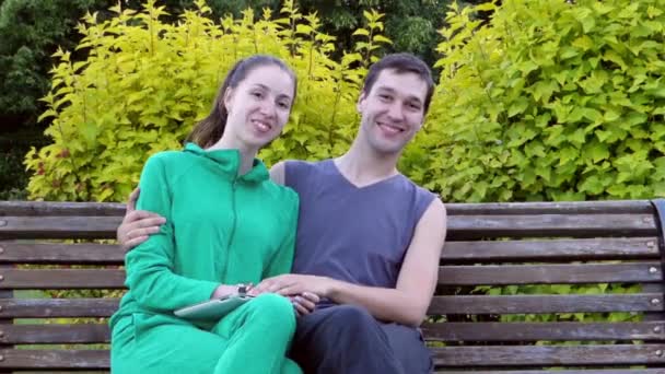 Beau jeune couple assis reposant sur un banc de parc. Ils s'embrassent et s'embrassent . — Video