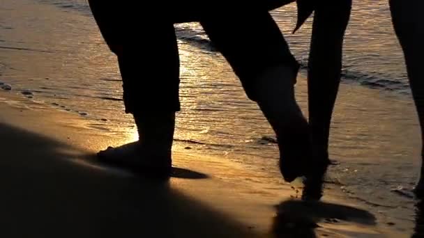 Silhuetten av benen i slow motion gå på stranden av havet under solnedgången. — Stockvideo