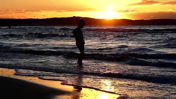 Jongetje permanent in de zee tijdens de zonsondergang en spelen met de golven. Slow Motion. — Stockvideo