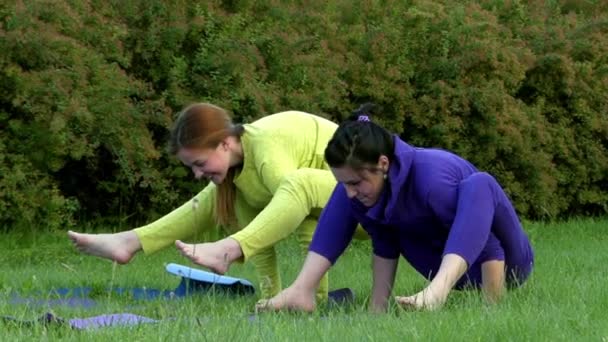 Yoga i parken. Två flickor försöker balansera på händerna. De faller ner och skratta. — Stockvideo