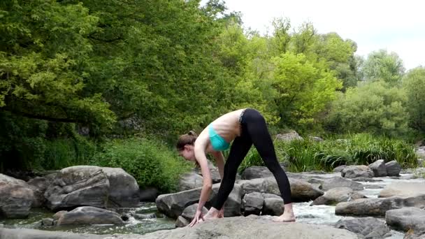 Молодая и спортивная девушка растягивает ногу на скале в середине горной реки . — стоковое видео