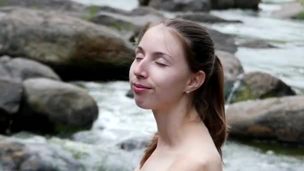 Het jonge meisje close-up. Zij inhaleert de frisse lucht met gesloten ogen en dan opent haar ogen glimlachend in de Camera. op de achtergrond berg rivier. — Stockvideo