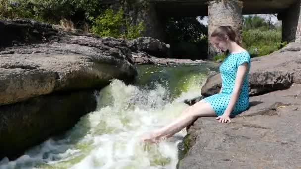 아름 다운 여자는 나머지 산 강 근처 돌에 앉아 있다. 그녀는 그의 발 및 재생 늦으면 물. — 비디오