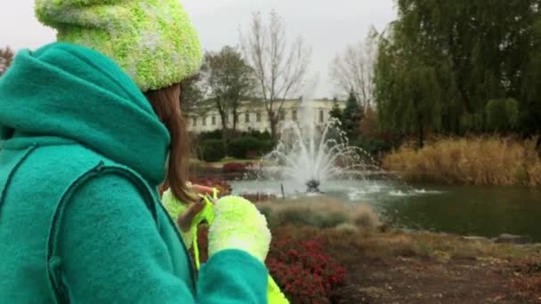 A menina de luvas verdes está tricotando um sentado no banco no parque . — Vídeo de Stock