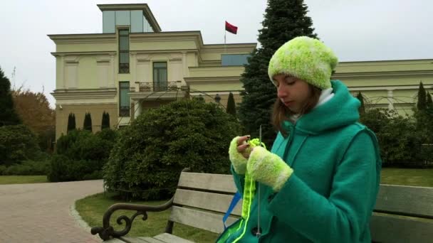 Das Mädchen in grünen Handschuhen strickt auf der Bank im Park. — Stockvideo